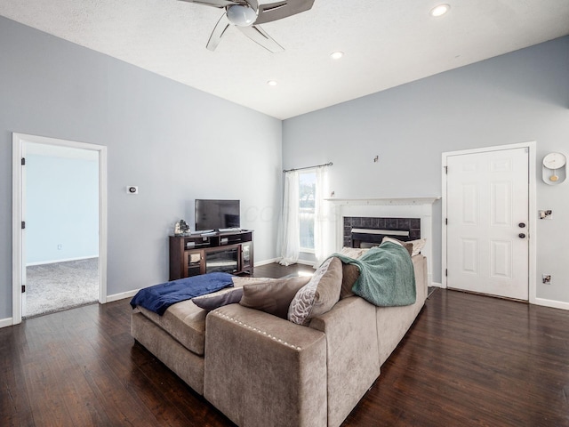 living room with a textured ceiling, dark wood-type flooring, a tiled fireplace, and ceiling fan