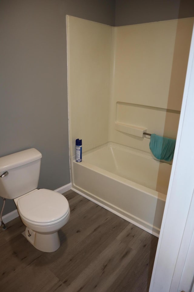 bathroom with washtub / shower combination, toilet, and hardwood / wood-style floors