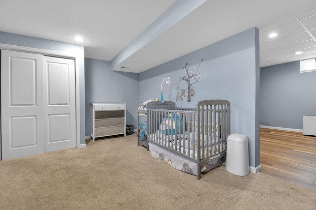 bedroom with a nursery area, a closet, a paneled ceiling, and light carpet