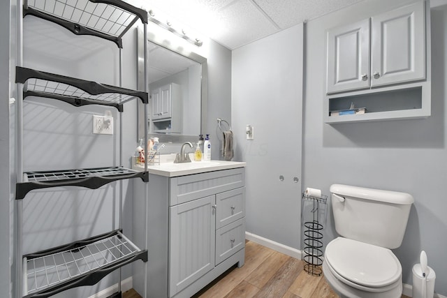 bathroom featuring wood-type flooring, a paneled ceiling, vanity, and toilet