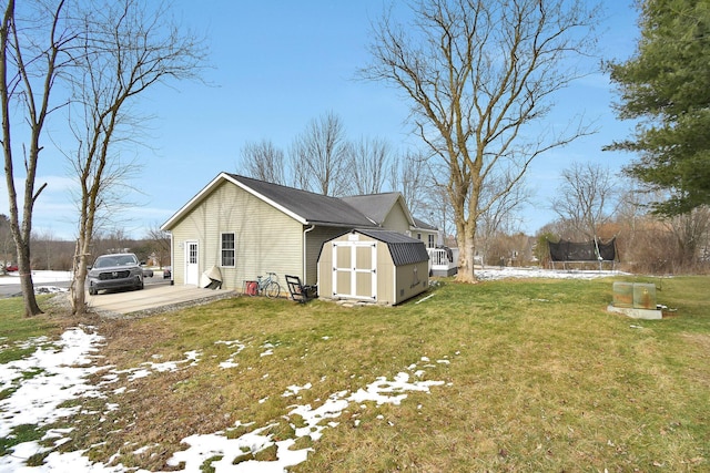 view of snow covered exterior with a trampoline, a lawn, and a storage unit