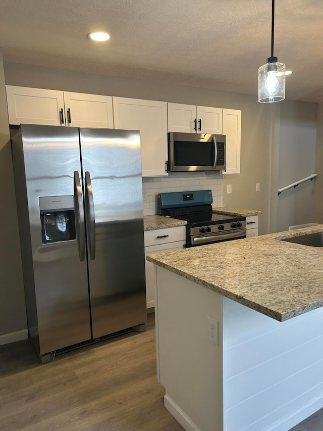 kitchen featuring white cabinetry, stainless steel appliances, tasteful backsplash, hanging light fixtures, and hardwood / wood-style flooring