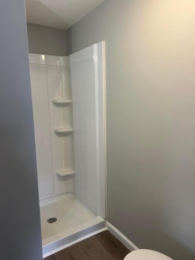 bathroom featuring a textured ceiling, toilet, a shower, and hardwood / wood-style flooring