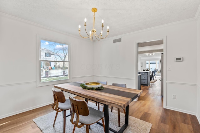 dining area with hardwood / wood-style floors, plenty of natural light, ornamental molding, a textured ceiling, and a chandelier