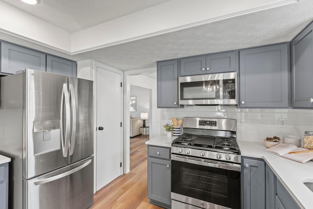 kitchen featuring gray cabinets, appliances with stainless steel finishes, decorative backsplash, a textured ceiling, and light hardwood / wood-style flooring