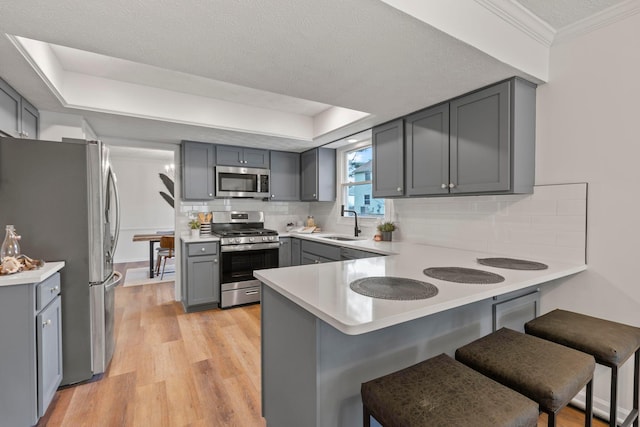 kitchen with a breakfast bar, sink, appliances with stainless steel finishes, gray cabinets, and kitchen peninsula