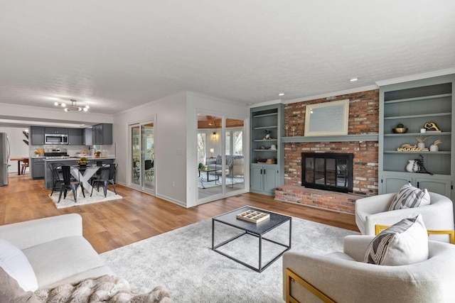 living room with built in features, crown molding, a brick fireplace, a textured ceiling, and light hardwood / wood-style flooring