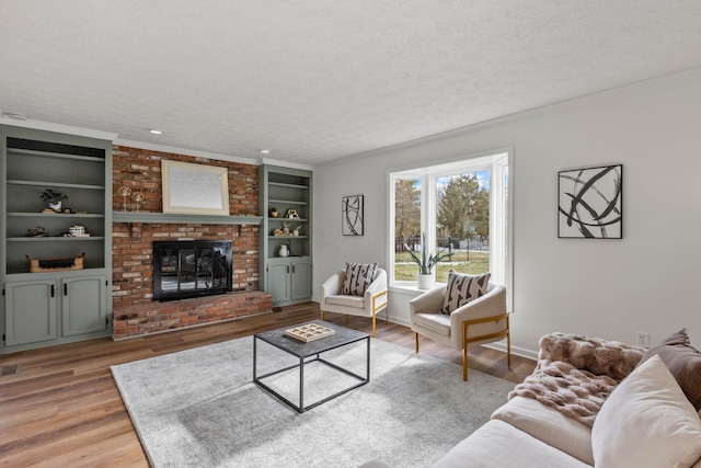 living room with a fireplace, crown molding, a textured ceiling, light wood-type flooring, and built in shelves