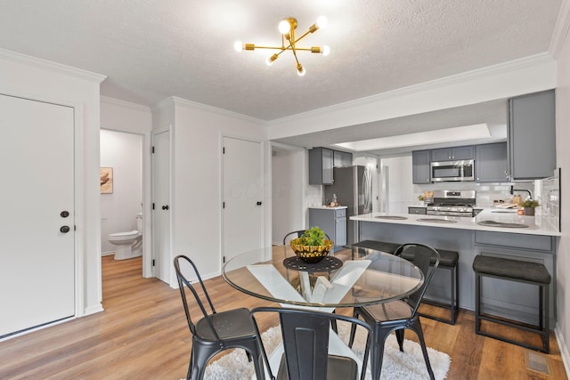 dining space featuring a notable chandelier, crown molding, a textured ceiling, and light wood-type flooring