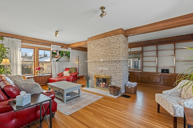 living room with light wood-type flooring, a brick fireplace, and beam ceiling