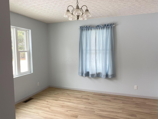 unfurnished room featuring light hardwood / wood-style floors, a textured ceiling, and an inviting chandelier