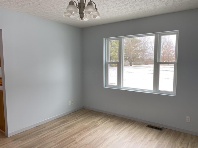 unfurnished room featuring light hardwood / wood-style floors, a textured ceiling, and an inviting chandelier