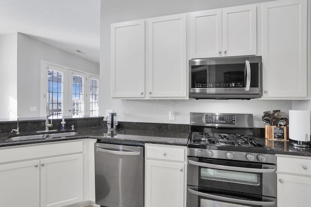 kitchen with sink, white cabinets, dark stone counters, and stainless steel appliances