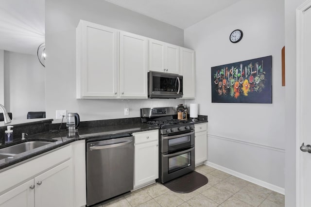 kitchen with appliances with stainless steel finishes, sink, white cabinets, light tile patterned floors, and dark stone countertops