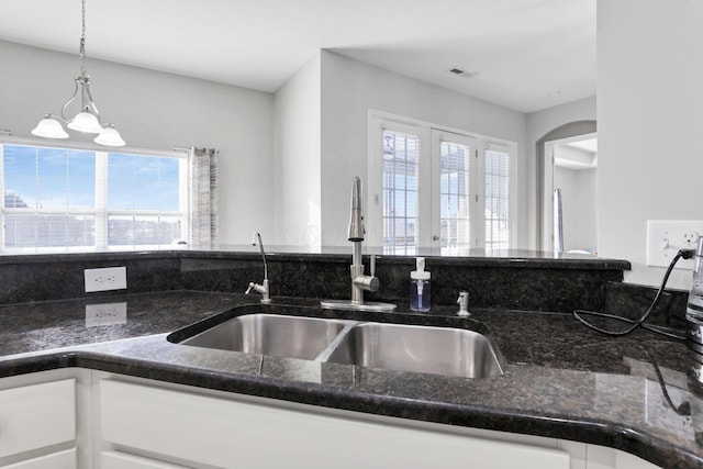 kitchen featuring decorative light fixtures, white cabinetry, dark stone counters, and a wealth of natural light