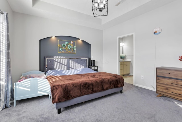 carpeted bedroom featuring ensuite bathroom and a raised ceiling