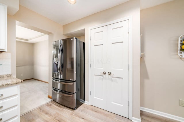 kitchen featuring stainless steel fridge, light stone countertops, white cabinets, and light wood-type flooring