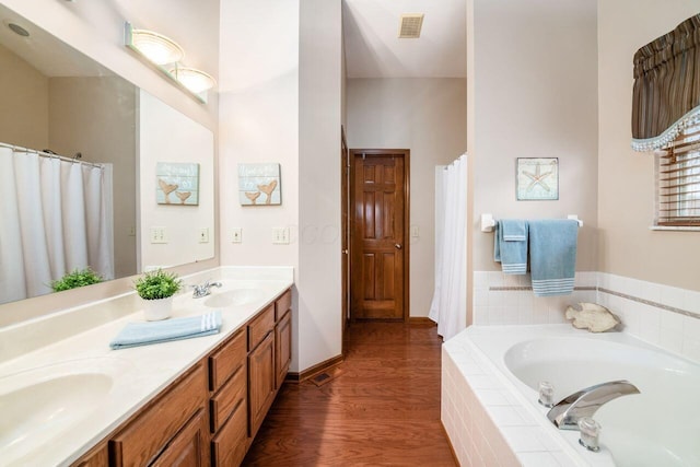 bathroom with vanity, wood-type flooring, and a relaxing tiled tub