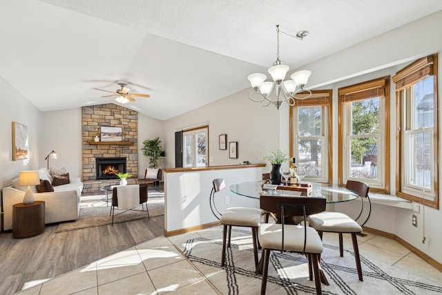 dining space with ceiling fan with notable chandelier, a stone fireplace, light tile patterned floors, and lofted ceiling