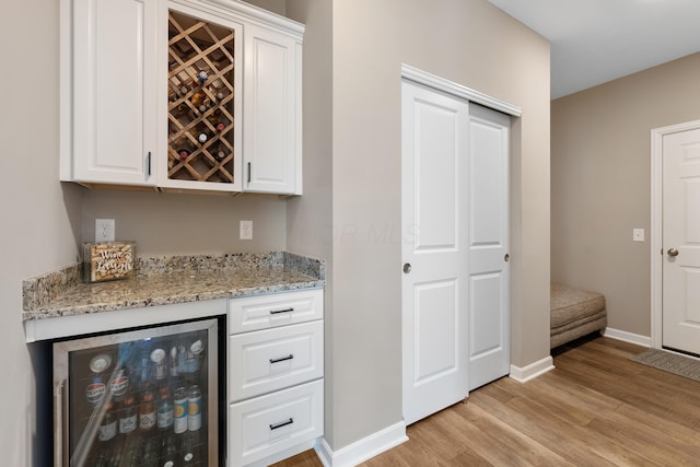 bar featuring light stone counters, white cabinets, light hardwood / wood-style flooring, and wine cooler