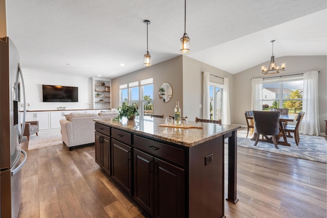 kitchen featuring light stone countertops, pendant lighting, a kitchen island, stainless steel refrigerator with ice dispenser, and dark brown cabinets