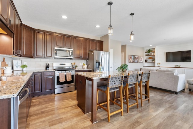 kitchen with sink, a kitchen island, pendant lighting, backsplash, and stainless steel appliances