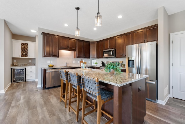 kitchen with wine cooler, hanging light fixtures, an island with sink, light hardwood / wood-style floors, and stainless steel appliances