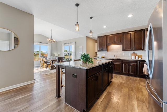 kitchen featuring light stone countertops, stainless steel refrigerator, a kitchen island, pendant lighting, and vaulted ceiling