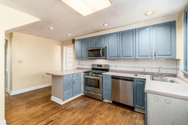 kitchen featuring blue cabinets, tasteful backsplash, appliances with stainless steel finishes, dark hardwood / wood-style flooring, and kitchen peninsula