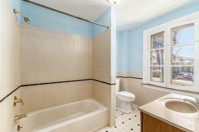 full bathroom with tiled shower / bath, tile walls, vanity, and toilet