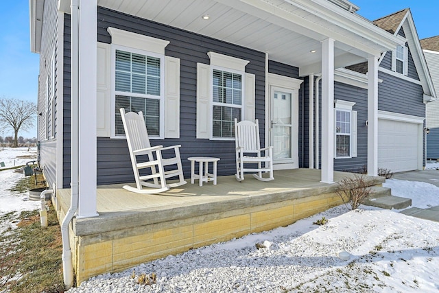 snow covered property entrance featuring covered porch and a garage