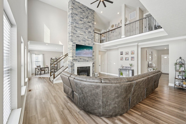 living room with ceiling fan, wood-type flooring, a stone fireplace, and a towering ceiling