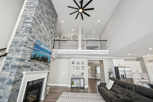 living room with a towering ceiling, dark wood-type flooring, a fireplace, ceiling fan, and crown molding