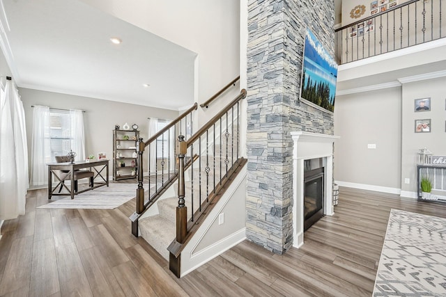 staircase featuring hardwood / wood-style flooring, a stone fireplace, ornamental molding, and a towering ceiling