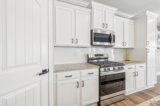 kitchen featuring light hardwood / wood-style floors, white cabinets, light stone counters, and appliances with stainless steel finishes