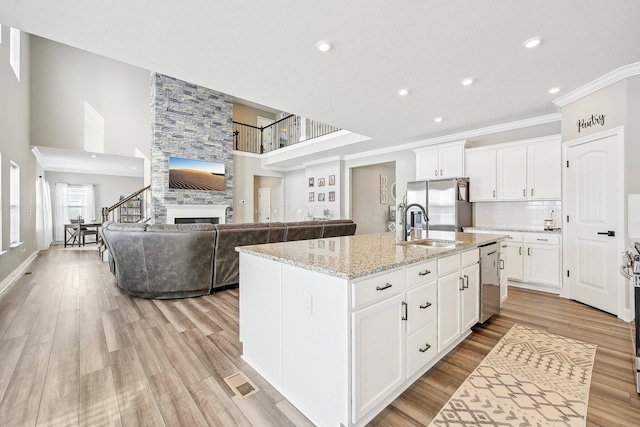 kitchen featuring light stone countertops, white cabinets, appliances with stainless steel finishes, sink, and a center island with sink