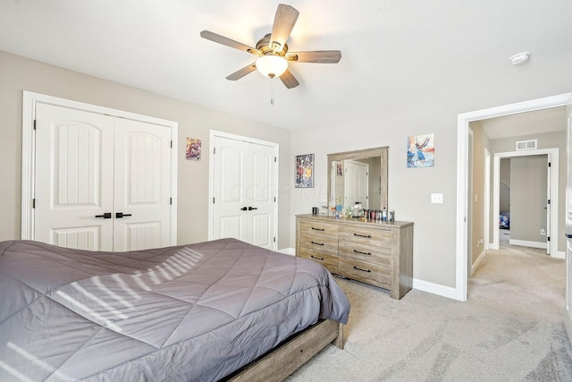 bedroom featuring light colored carpet, two closets, and ceiling fan