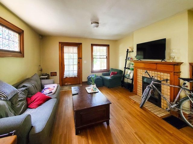 living room with a tiled fireplace and light wood-type flooring