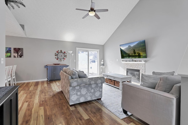 living room with a textured ceiling, wood-type flooring, a tiled fireplace, ceiling fan, and lofted ceiling