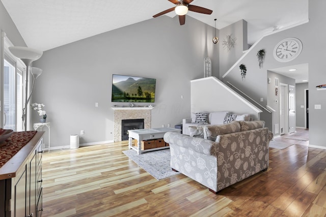 living room featuring ceiling fan, high vaulted ceiling, a tile fireplace, and wood-type flooring