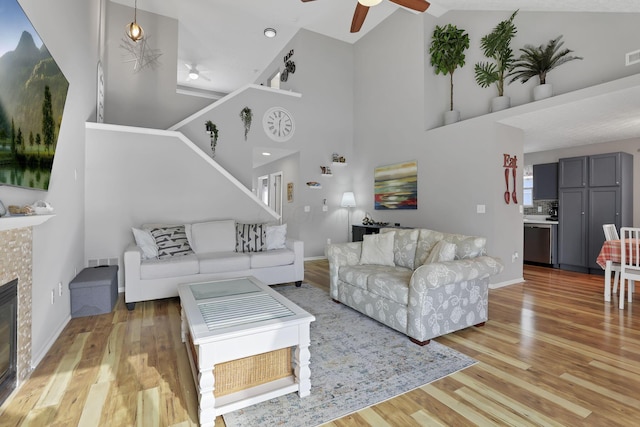 living room with a tile fireplace, light hardwood / wood-style floors, high vaulted ceiling, and ceiling fan