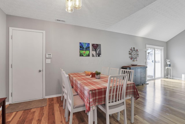 dining room with hardwood / wood-style floors, a textured ceiling, and vaulted ceiling