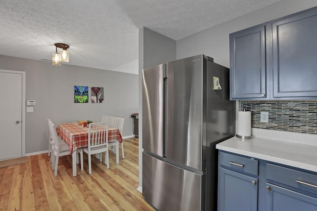 kitchen featuring a textured ceiling, tasteful backsplash, light hardwood / wood-style floors, stainless steel fridge, and blue cabinets