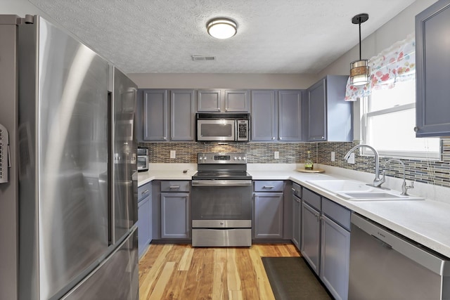 kitchen with decorative light fixtures, stainless steel appliances, sink, gray cabinets, and light wood-type flooring