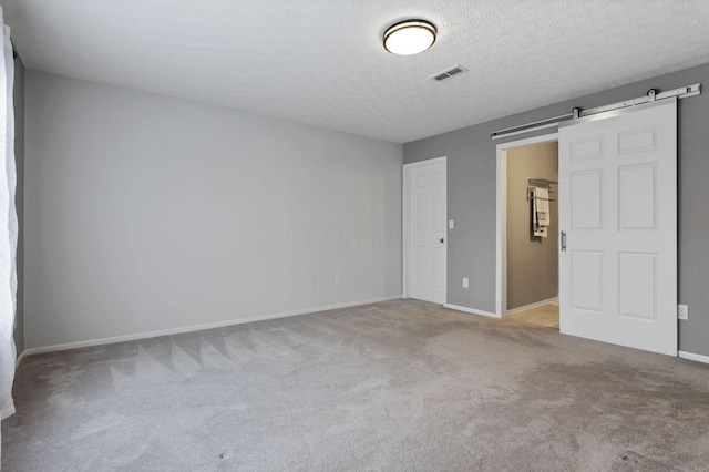 carpeted spare room with a textured ceiling and a barn door