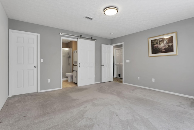 unfurnished bedroom featuring a barn door, light colored carpet, a textured ceiling, and ensuite bath