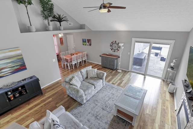 living room with a textured ceiling, light hardwood / wood-style flooring, lofted ceiling, and ceiling fan