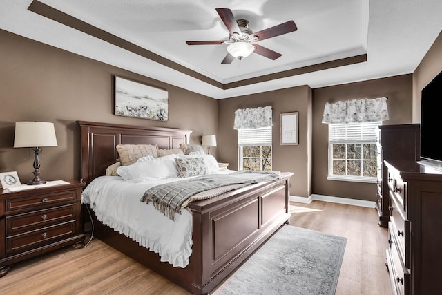 bedroom featuring a ceiling fan, a raised ceiling, light wood-style flooring, and baseboards