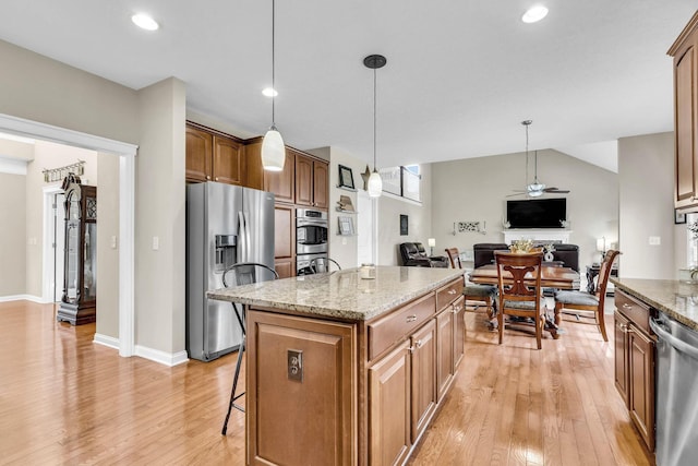 kitchen with light stone counters, a center island, brown cabinets, stainless steel appliances, and hanging light fixtures