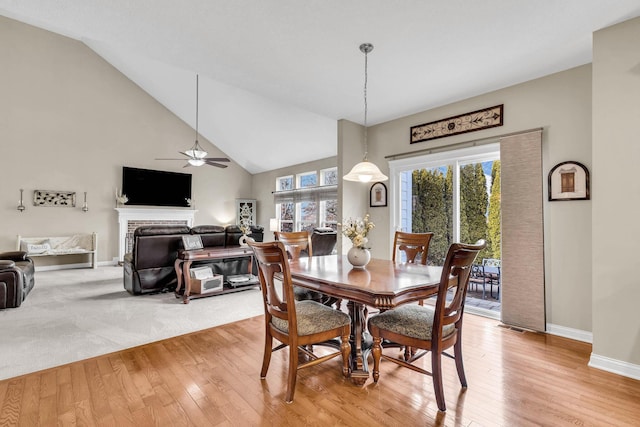 dining space featuring a fireplace, light wood finished floors, visible vents, high vaulted ceiling, and baseboards